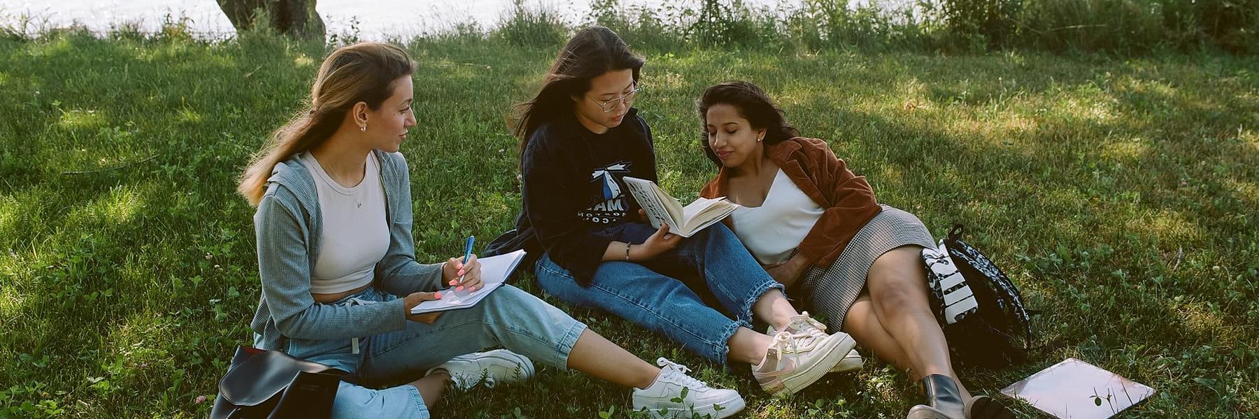 Three students study on campus outside under a tree.